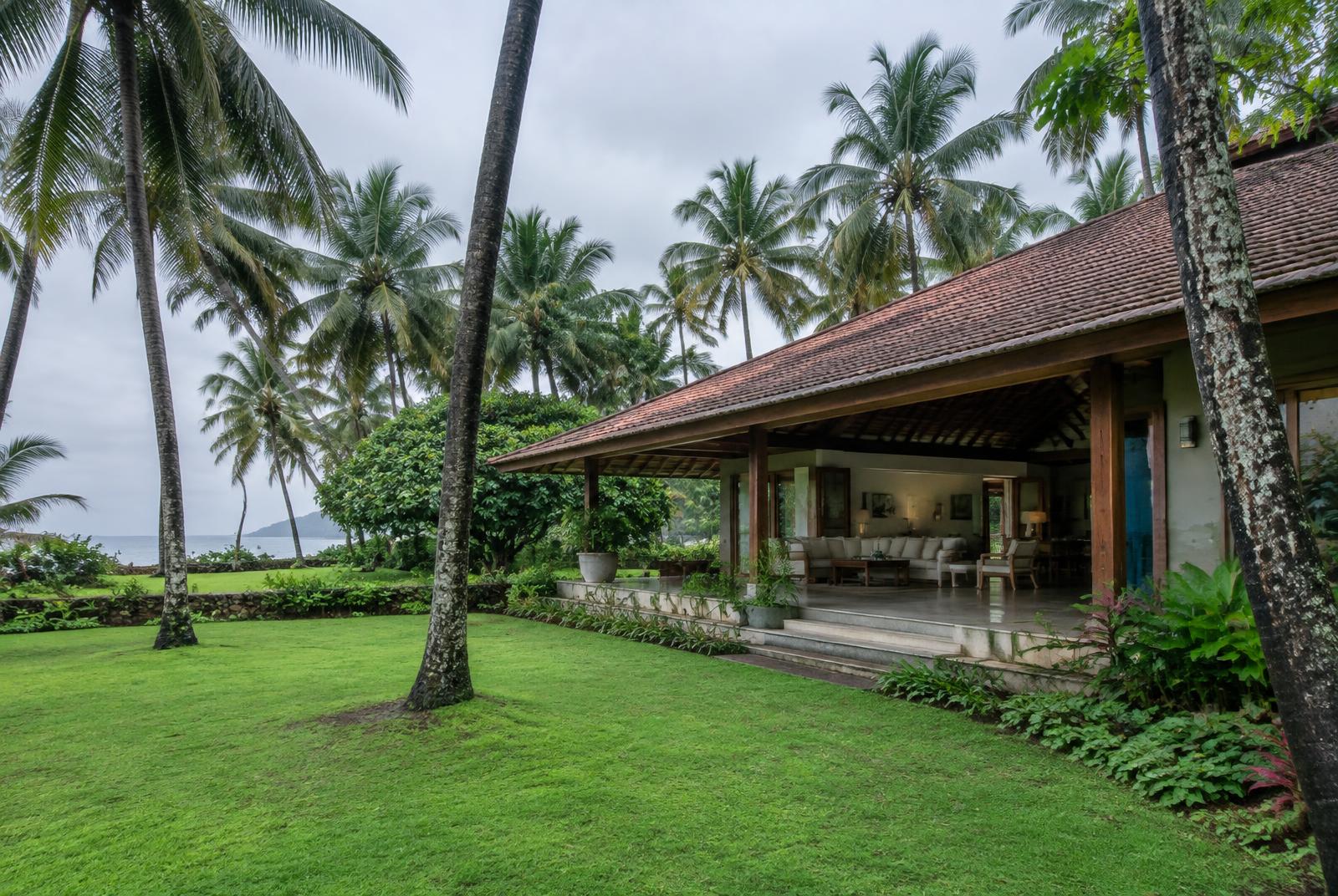 Open timber living pavilion under a clay-tile roof among coconut palms