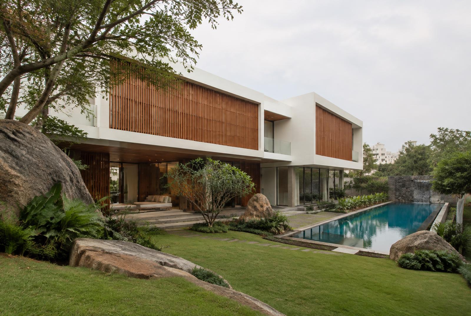White villa with teak louvres beside a lap pool and granite boulders